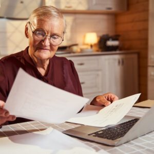 Elderly woman checking documents in front of the laptop
