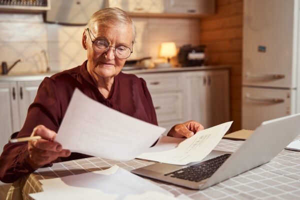 Elderly woman checking documents in front of the laptop